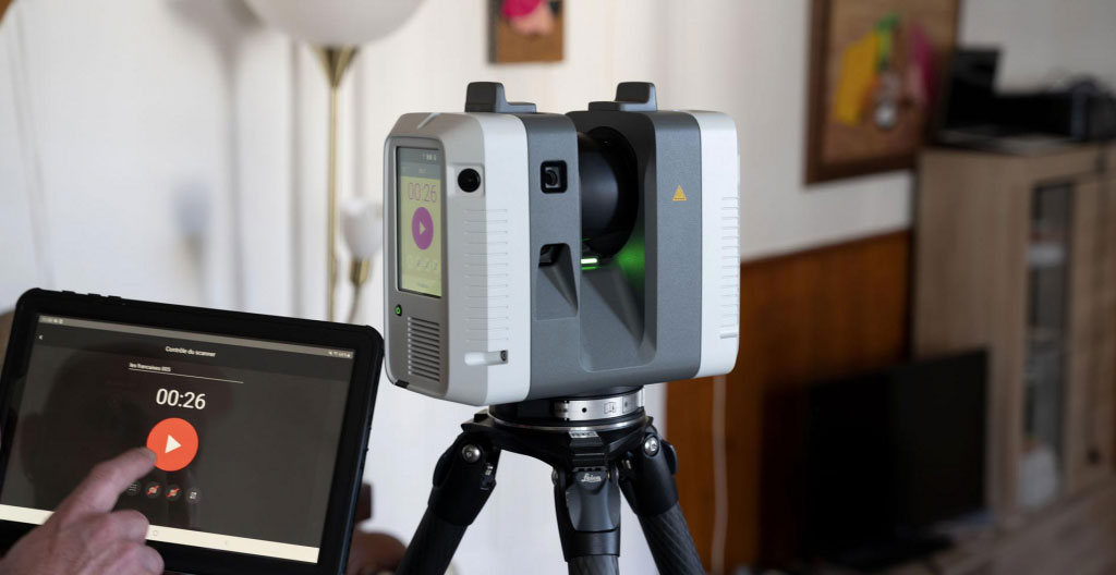 Technicien mesurant une ouverture de fenêtre dans un bâti ancien avec télémètre laser, murs en pierre apparente révélant irrégularités dimensionnelles